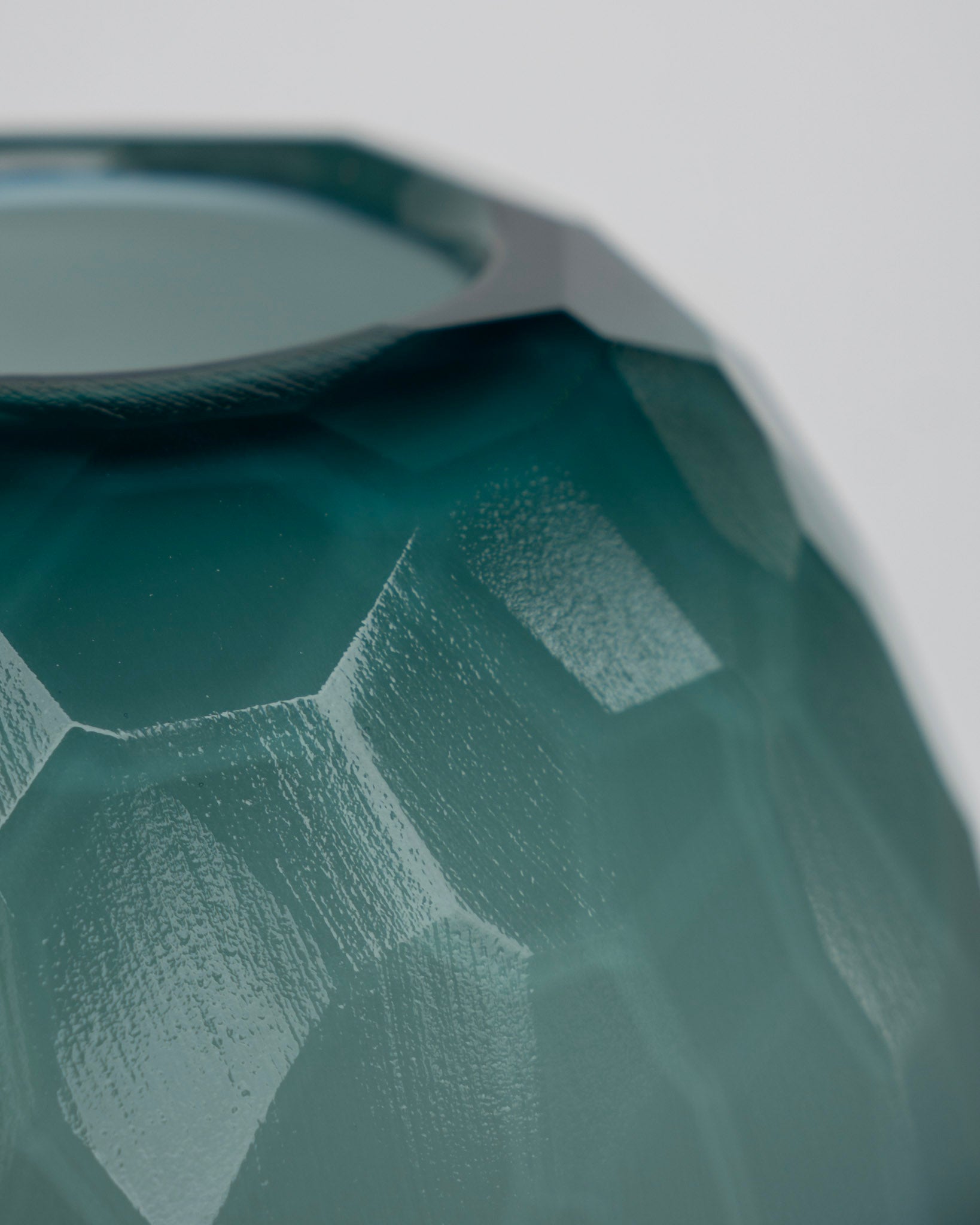 Kant på grønn fasettert vase med geometriske flater og grå detaljer