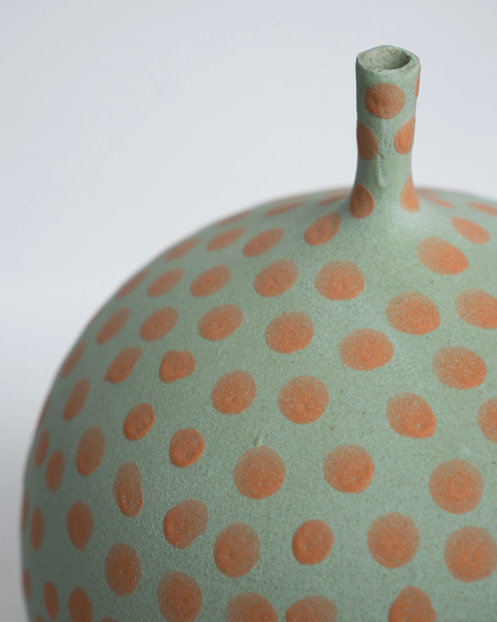 Keramisk vase i lysegrøn med orange prikker og smal hals