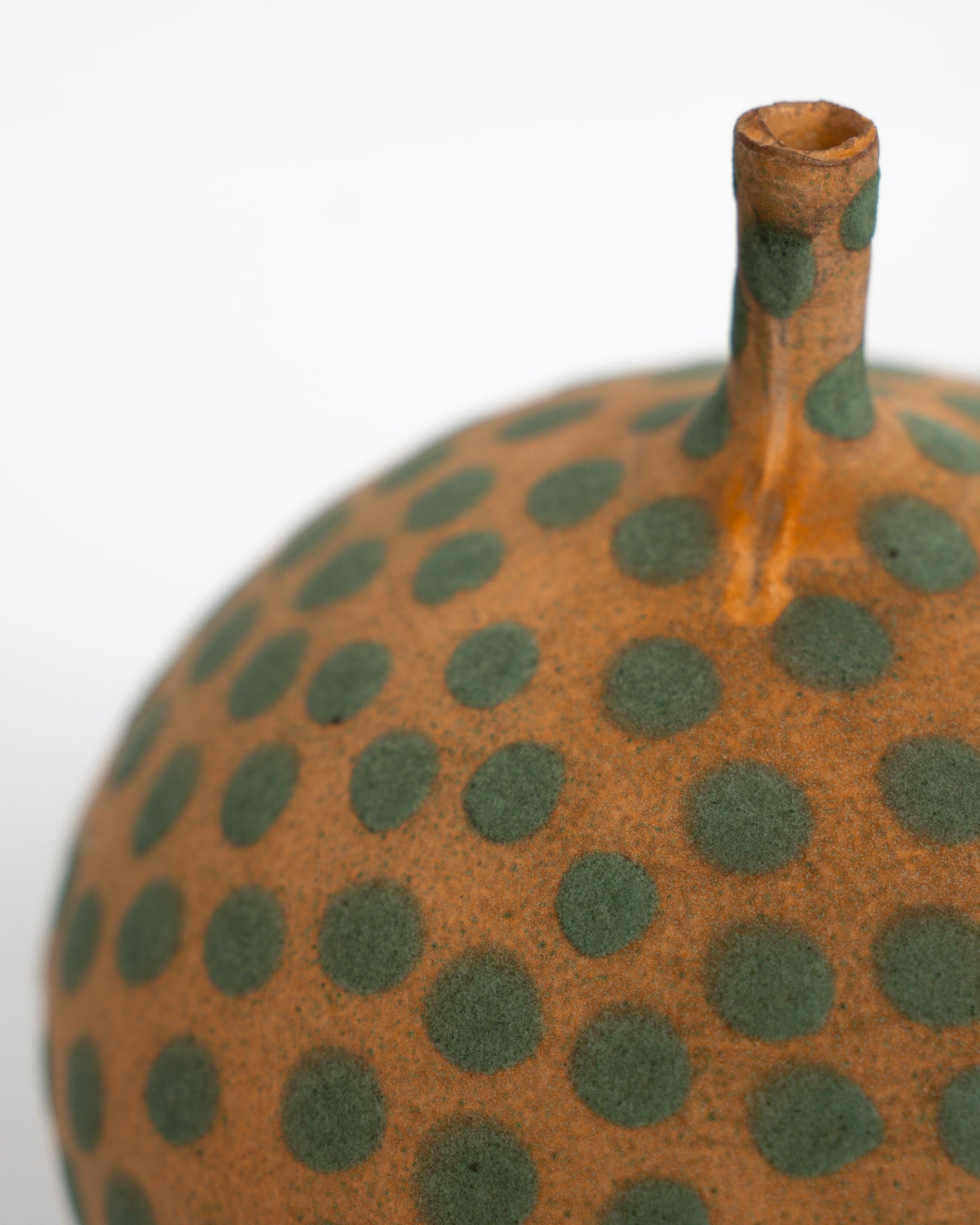 Keramisk vase, nærbilde av smal hals og oransje overflate med grønne prikker