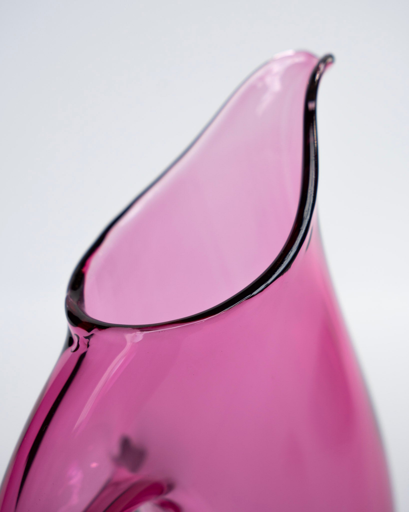 Nærbilde av rosa fløtemugge i glass med buet svart kant og åpen tut
