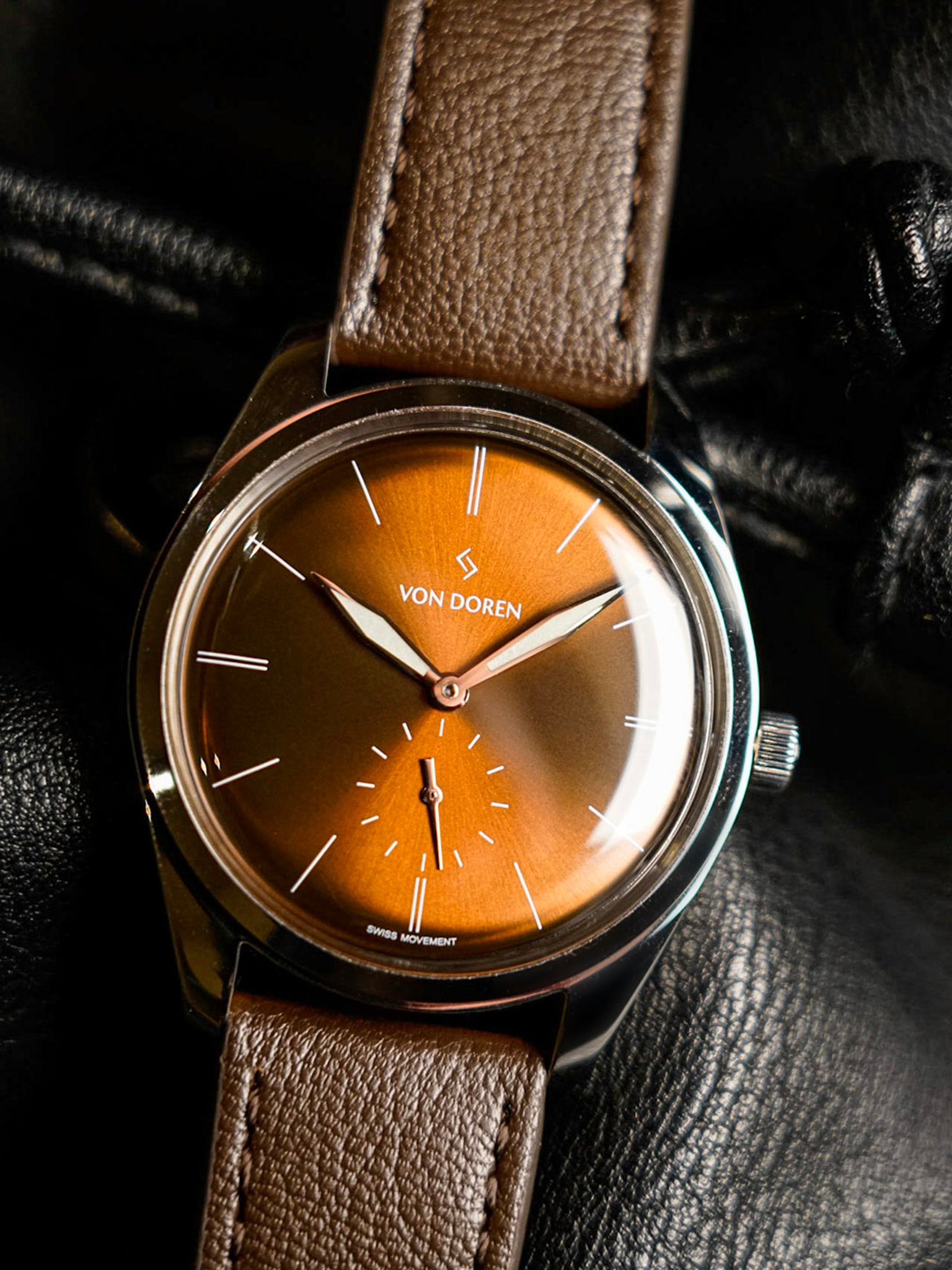 Rundt armbåndsur med mørk brun lærrem og varm oransje skive.