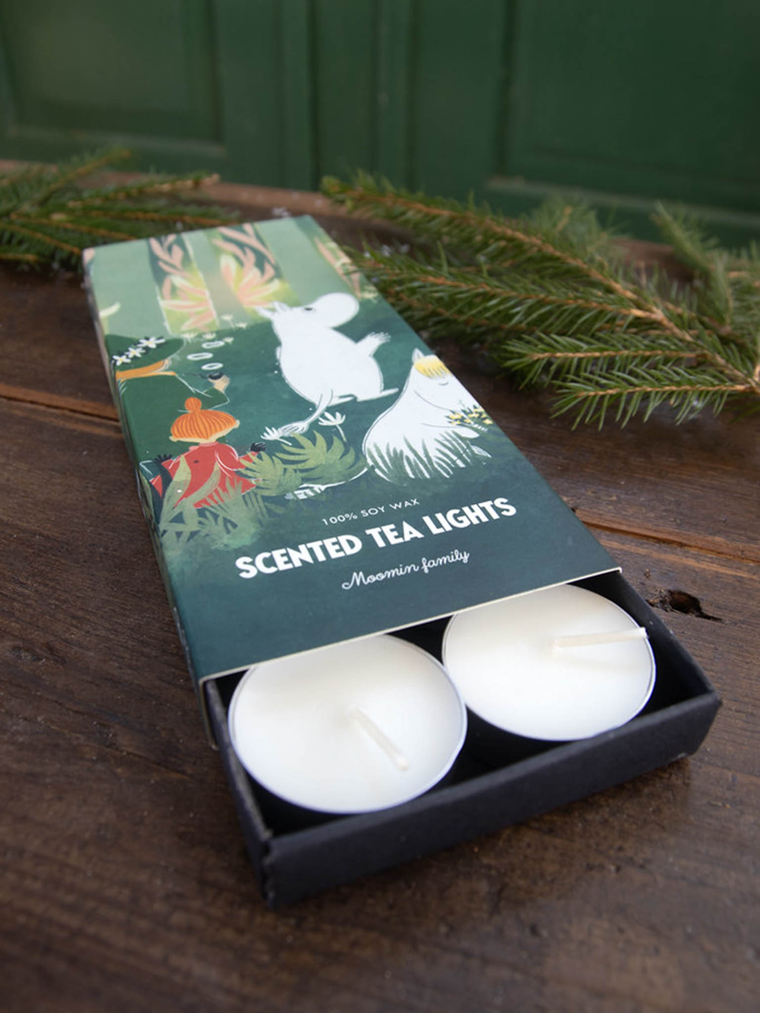 Duftende telys i eske på treflate, Moomin-familieillustrasjon og telys synlige