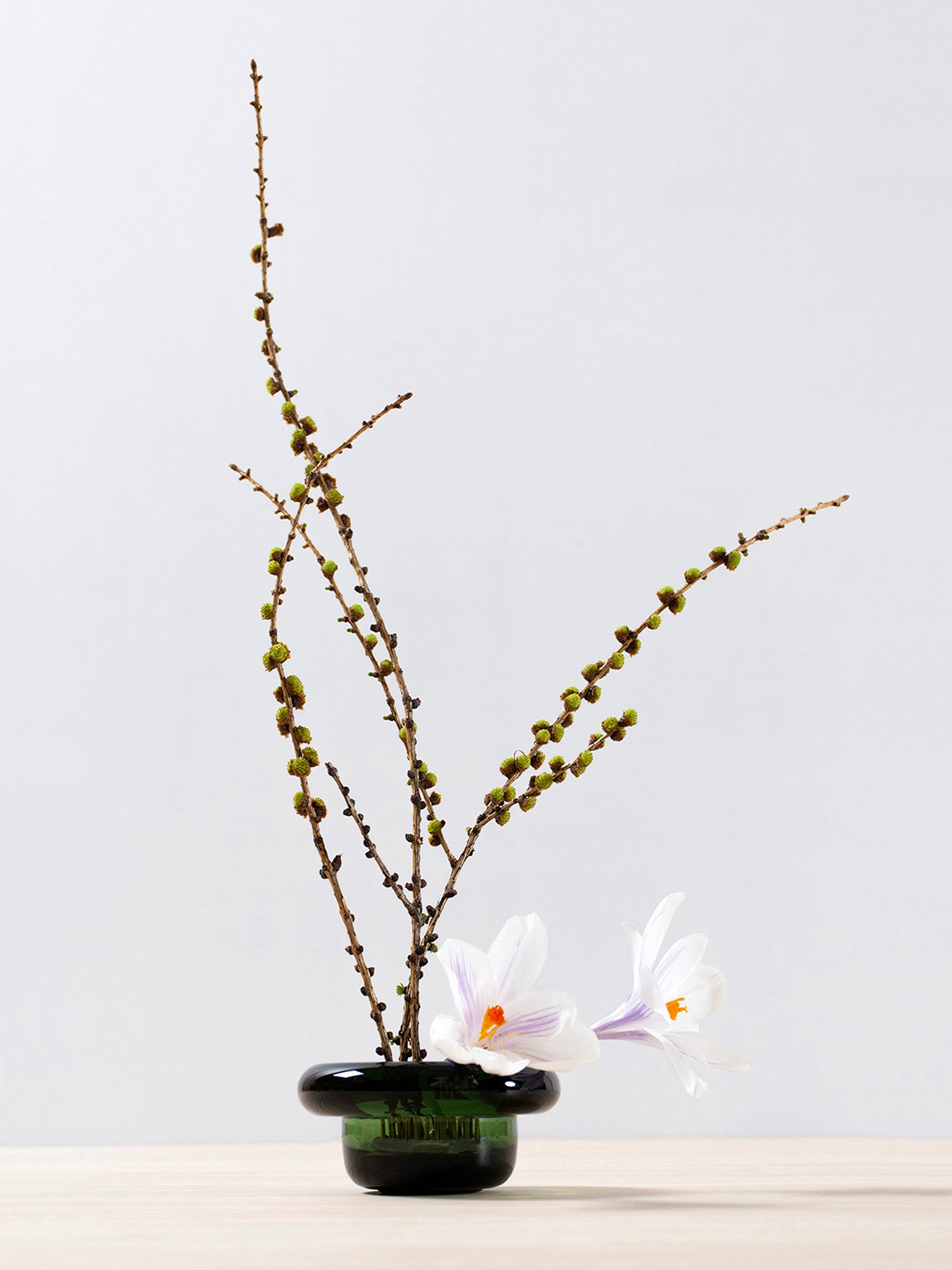 Grønn sirkel-lysholder i glass med kvister og hvite blomster.