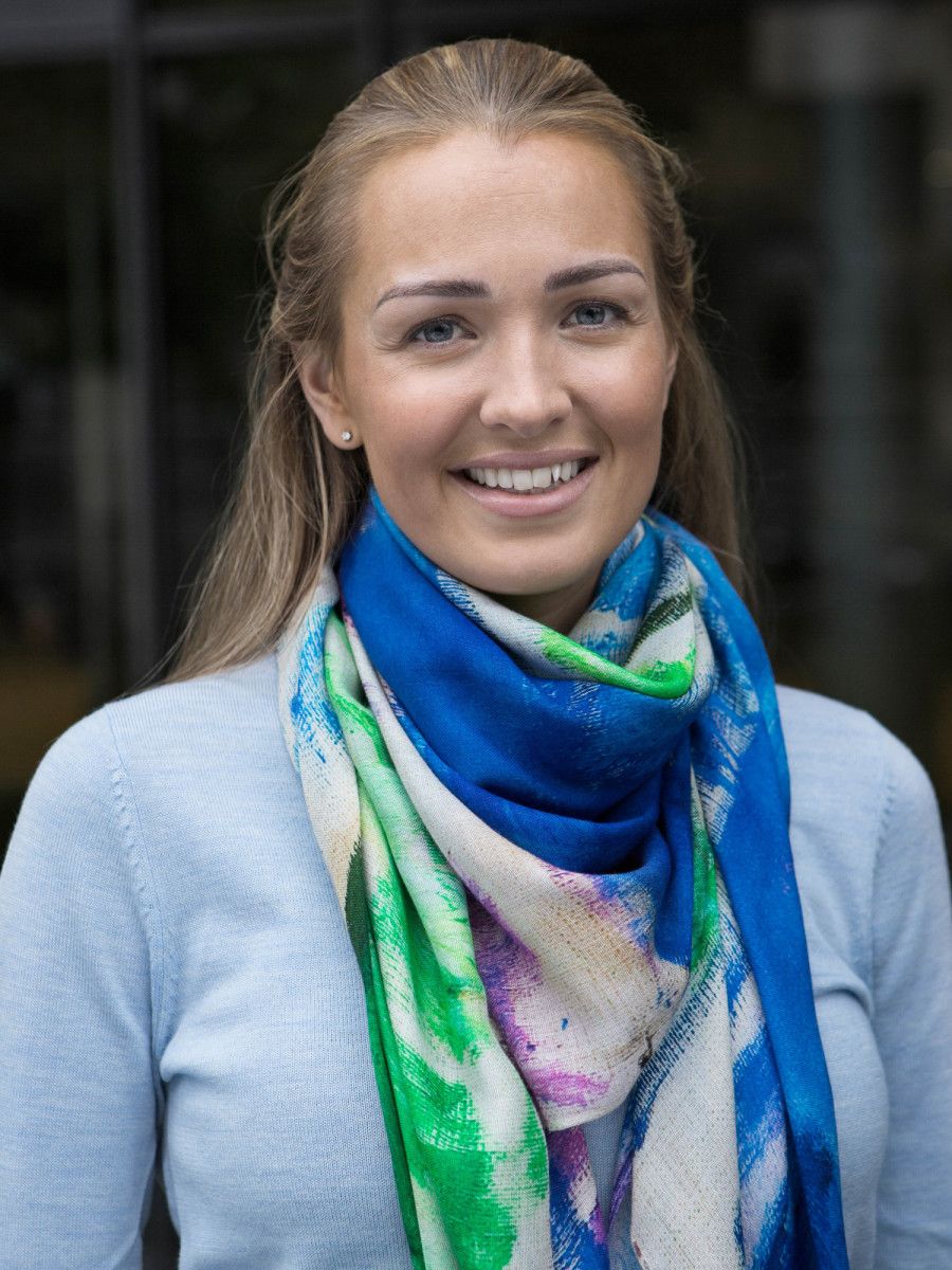 Flerfarvet skjerf i blå, grønn og lilla med bølgemønster, rundt halsen