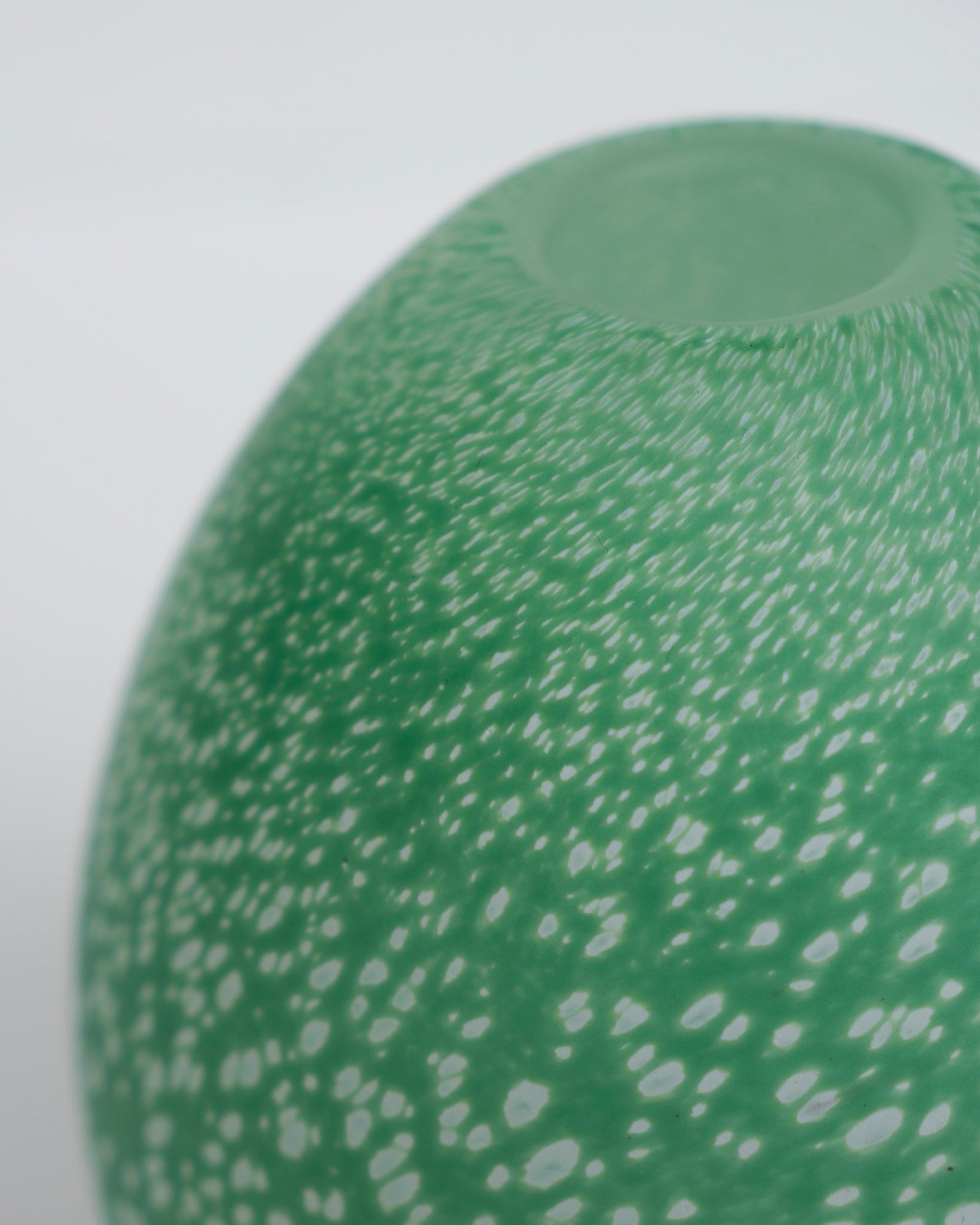 Grønn eggevase med avrundet åpning og hvite prikker på spekket overflate.