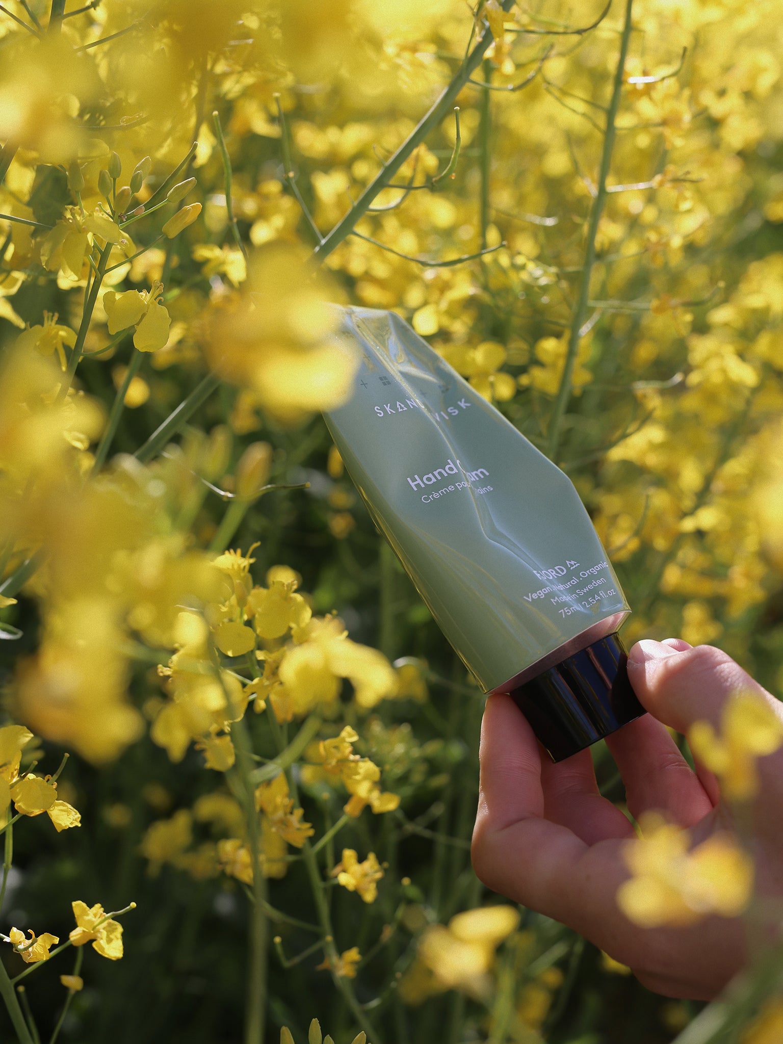 FJORD håndkremtube i lys grønn holdt i hånd mot gule blomster