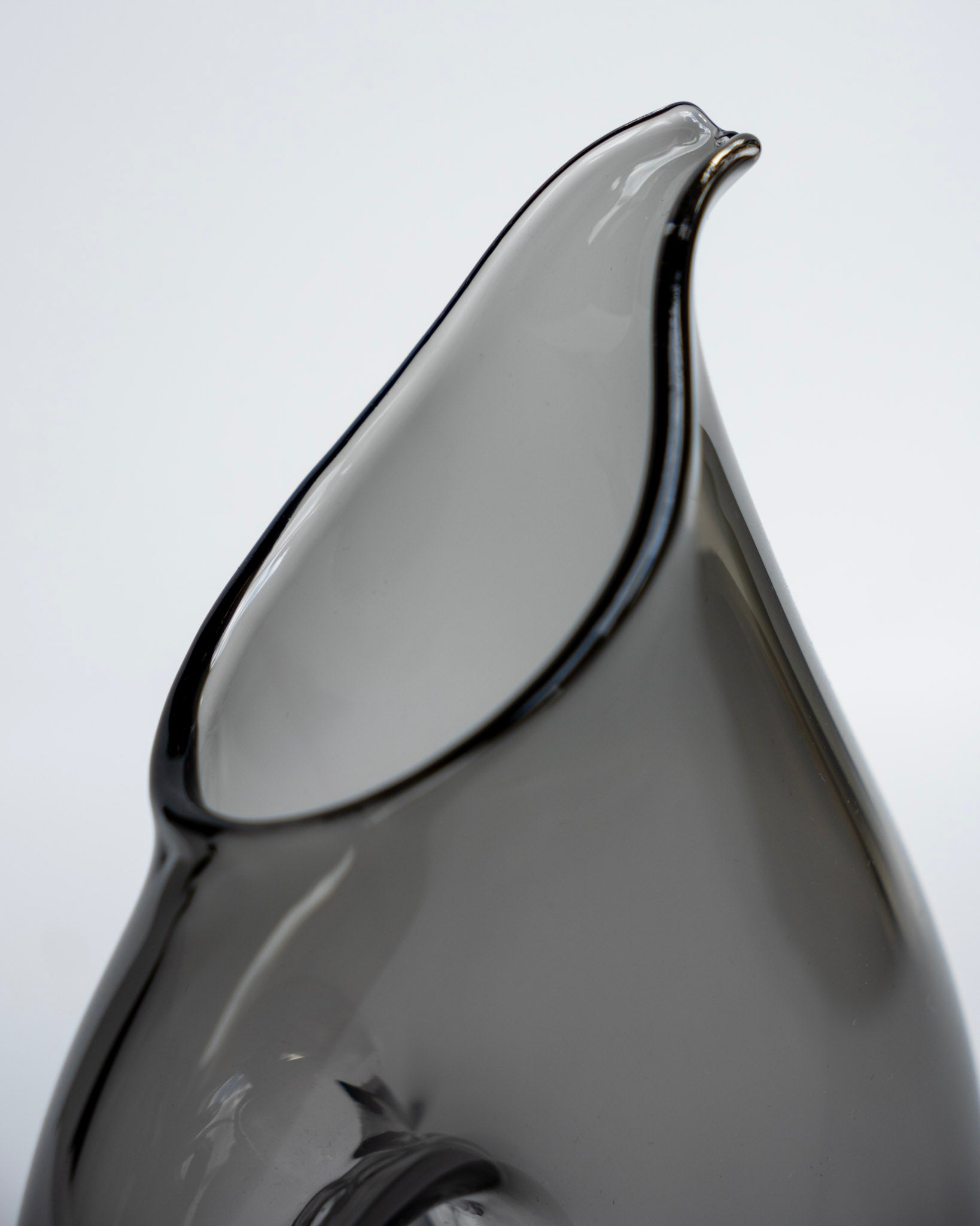 Svart fløtemugge, nærbilde av tut og blank, glassaktig overflate.