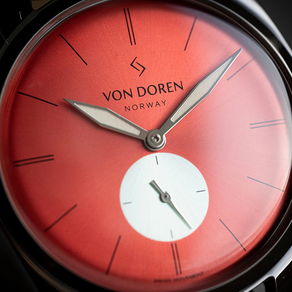 Detalj av rød urskive med VON DOREN-logo, sølvvisere og hvit sekundskive