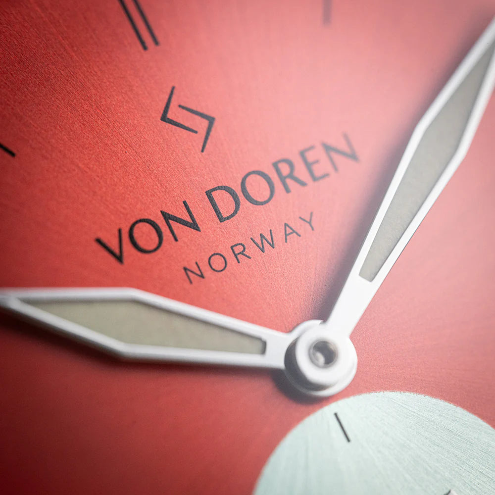 Nærbilde av rød urskive med VON DOREN NORWAY-logo og sølv timeviser