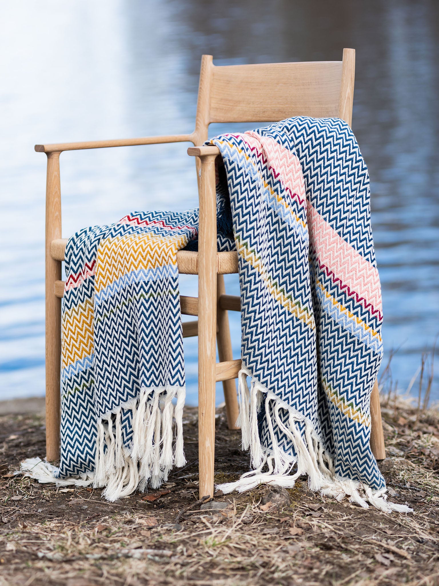 Blått bunadspledd med sikksakkmønster, frynser og flerfargede striper på trestol
