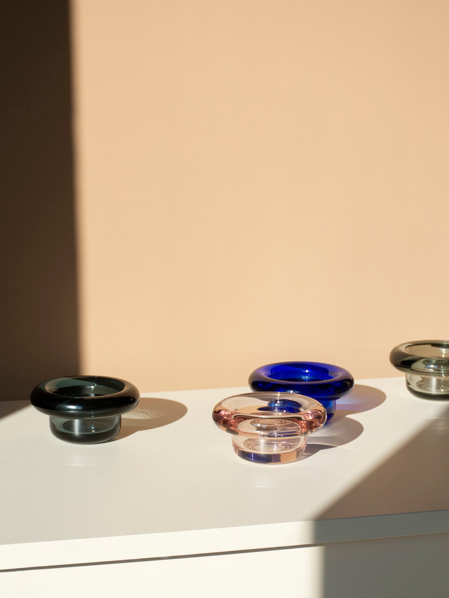 Sirkel-lysestaker i blått, mørkegrønt og gjennomsiktig glass på hylle