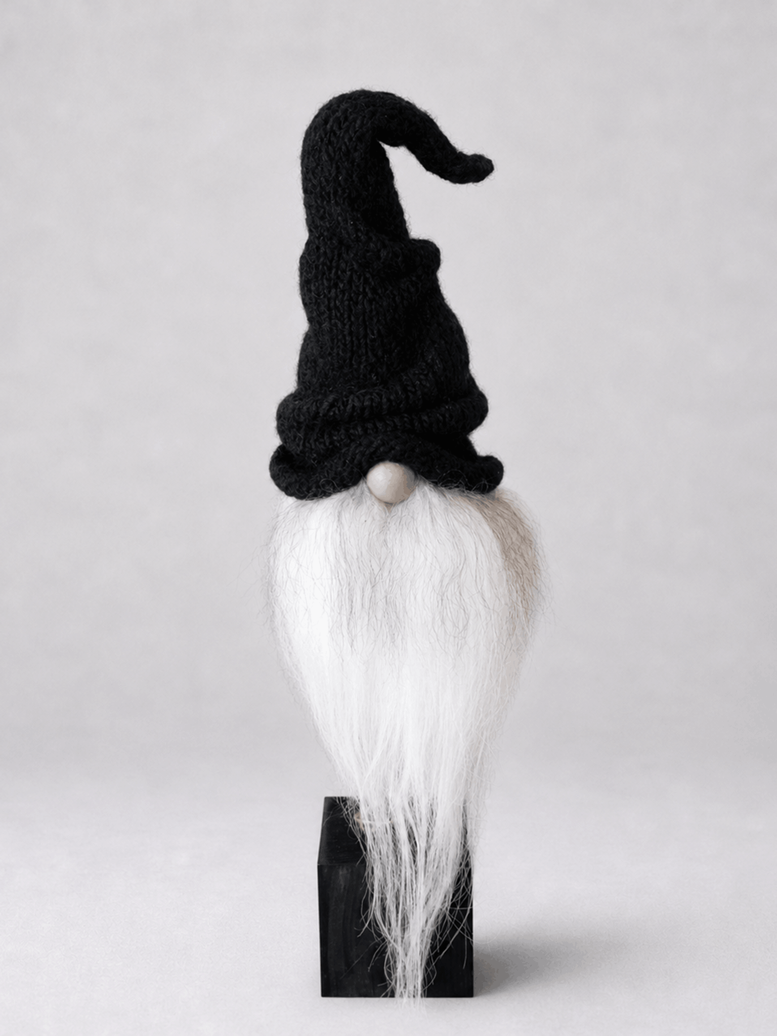 Svart nissefigur med strikket hatt og langt hvitt skjegg på svart sokkel
